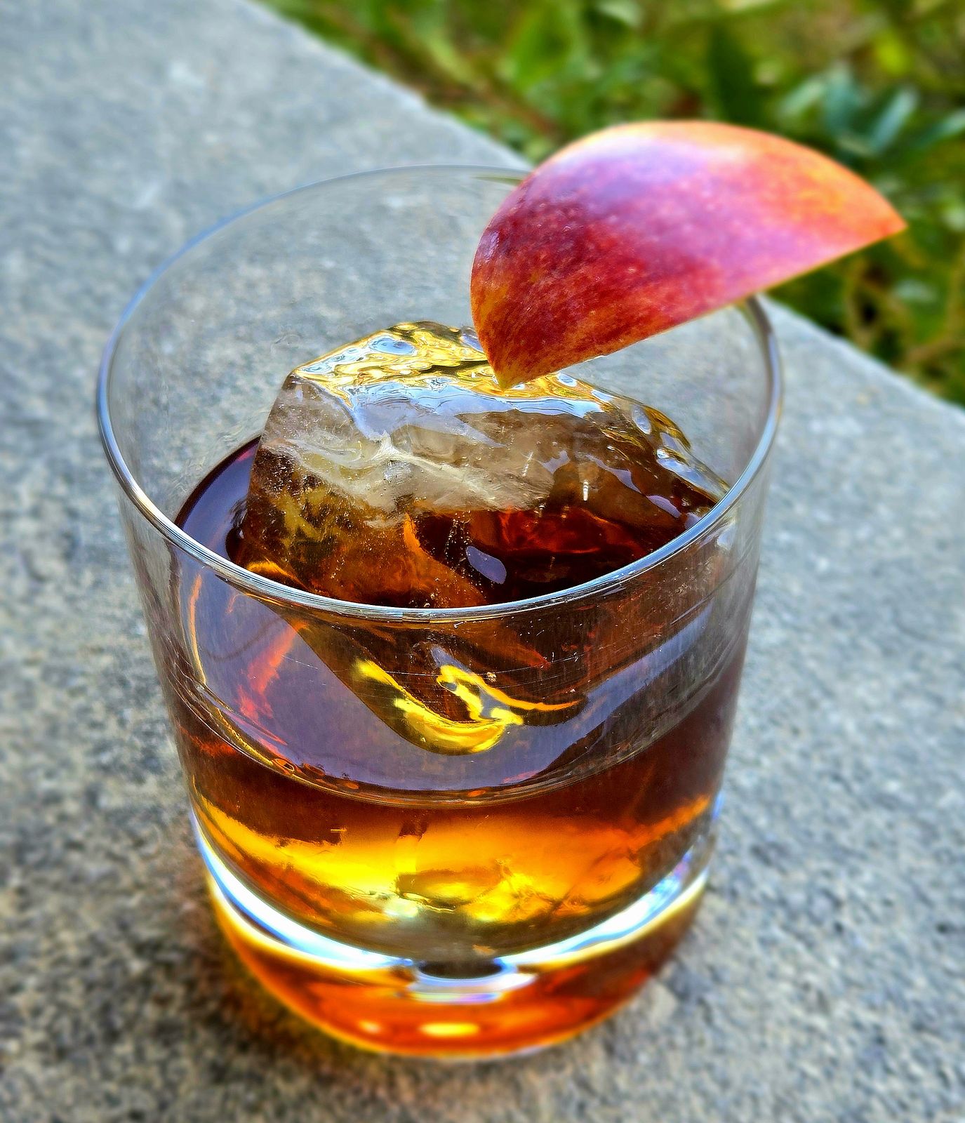 Festival Apple cocktail in a rocks glass with apple wedge garnish atop a stone wall.