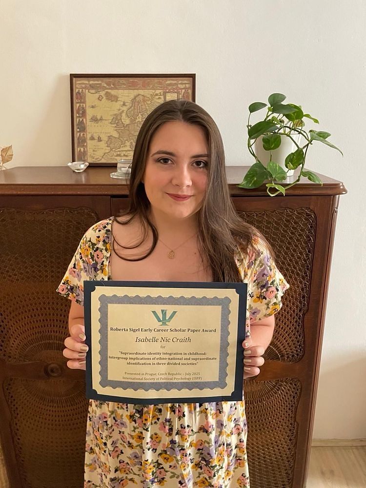 Isabelle holding her award certificate, reading: “Roberta Sigel Early Career Scholar Paper Award Isabelle Nic Craith for "Supraordinate identity integration in childhood: Intergroup implications of ethno-national and supraordinate identification in three divided societies"  Presented in Prague, Czech Republic - July 2025 International Society of Political Psychology (ISPP)