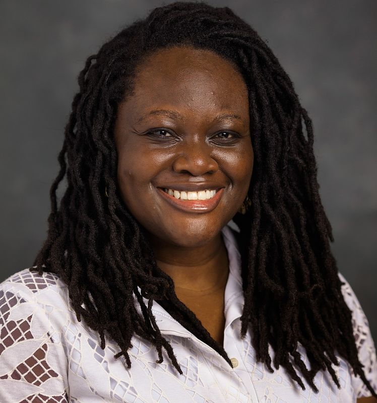 Headshot of Belinda Akpa. She smiles at the camera, wearing a white dress.