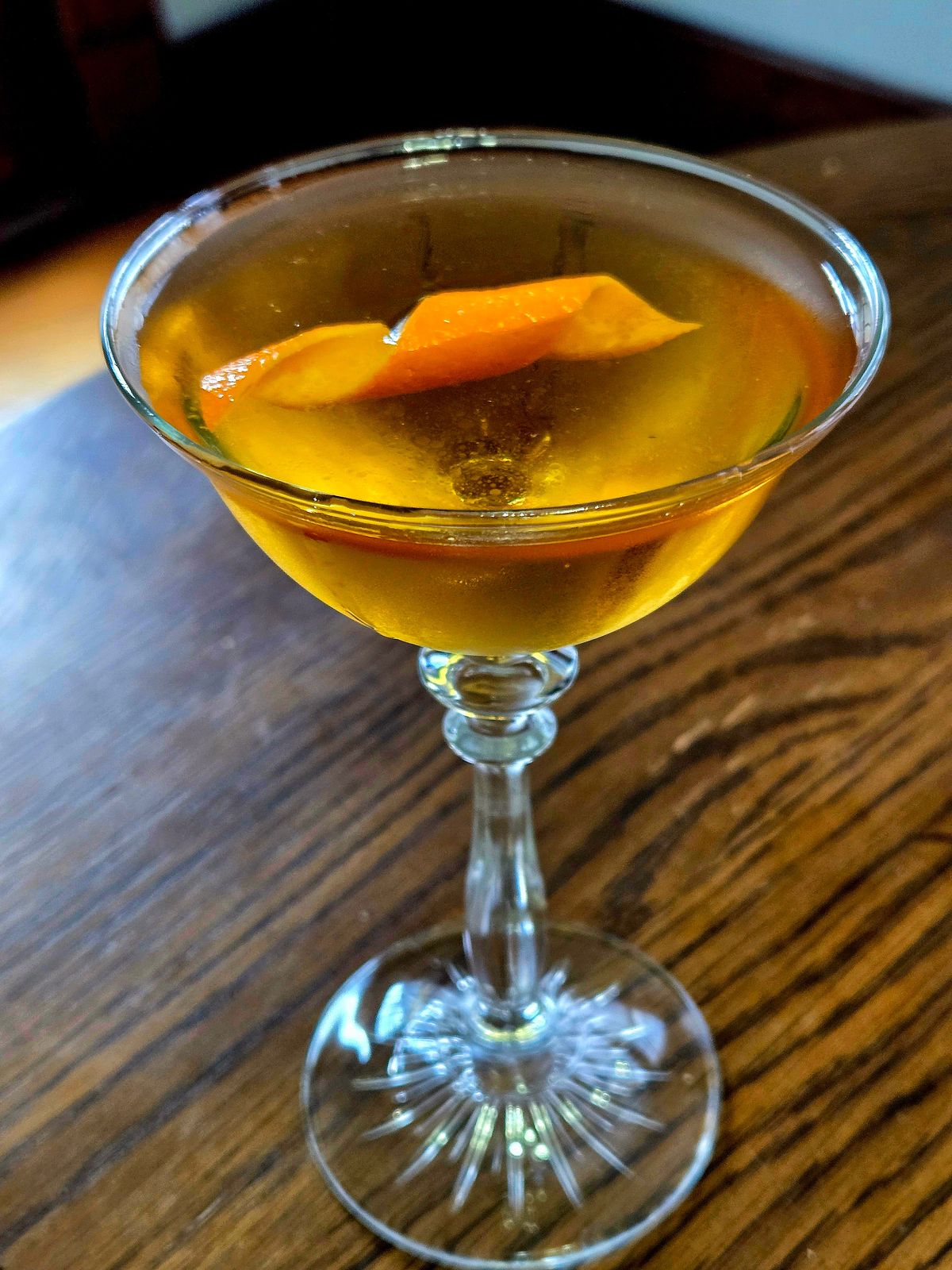 An Angel Face cocktail sitting in a coupe glass with orange twist sitting atop a wooden table.