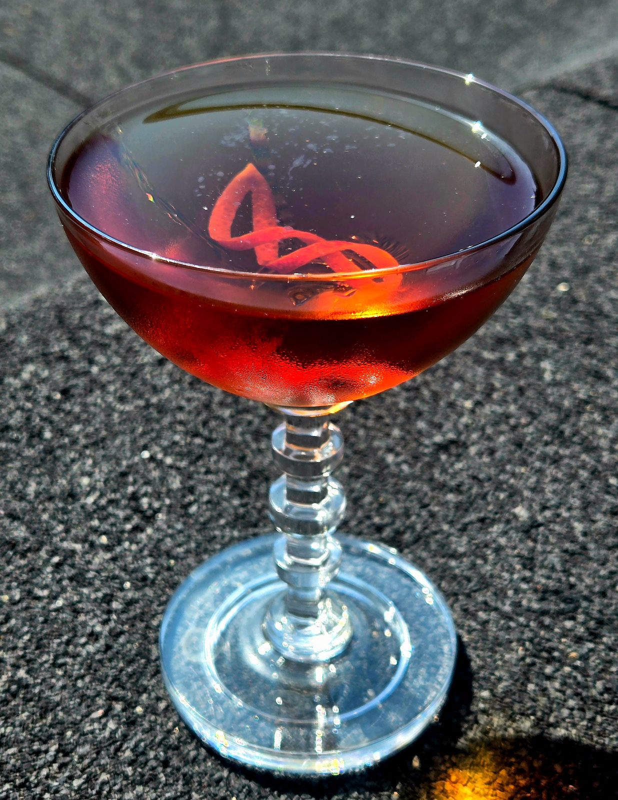 An Adonis cocktail in a champage coupe with orange lattice garnish sitting on a sunny rooftop..