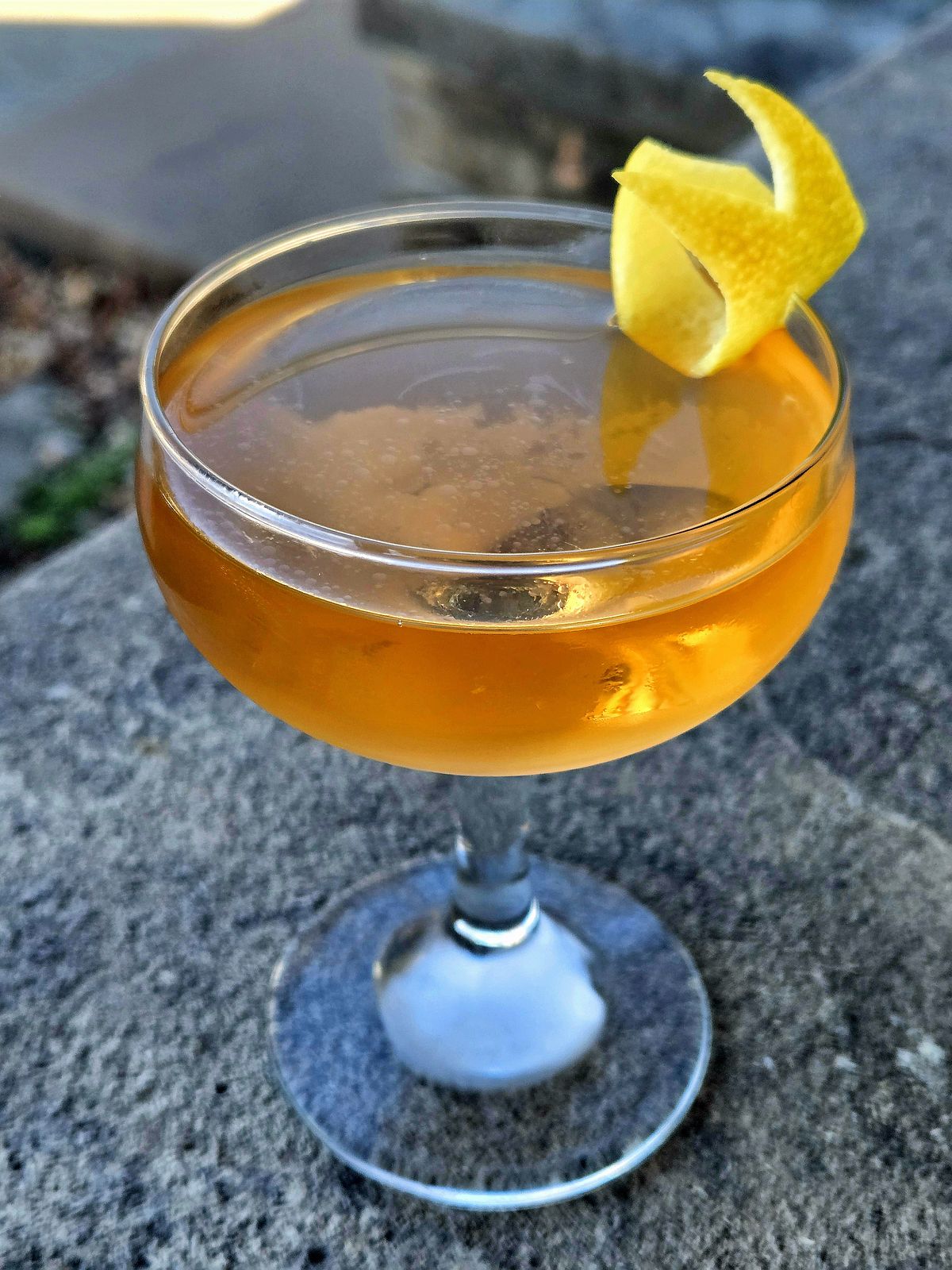 Original Tuxedo with lemon twist in a Coupe atop a stone wall.