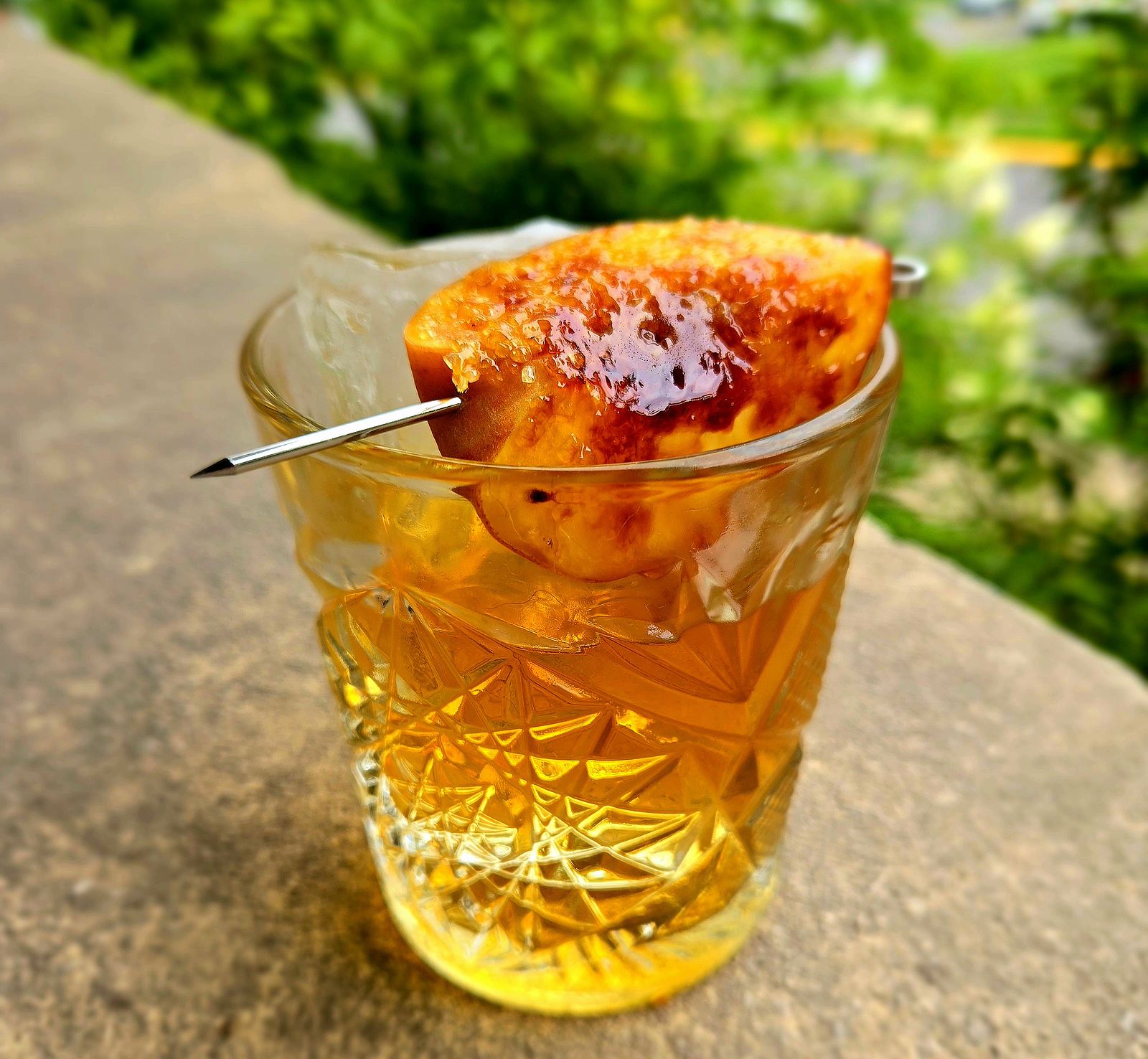 Tom's Tiki Triple rum old-fashioned with brûléed peach garnish in a rocks glass atop a stone wall.