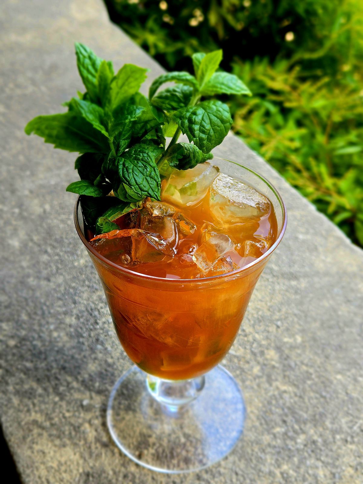 Jasper's Planter's Punch in a vintage wine glass with mint sprig garnish atop a stone wall.