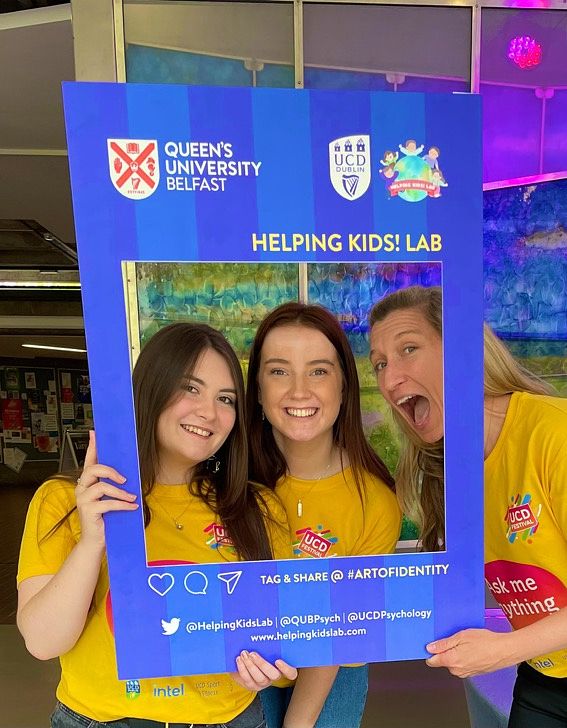 Isabelle Nic Craith, Dearbháile Counihan and Laura K. Taylor are seen holding a frame around their faces, smiling. All are wearing yellow t-shirts.
