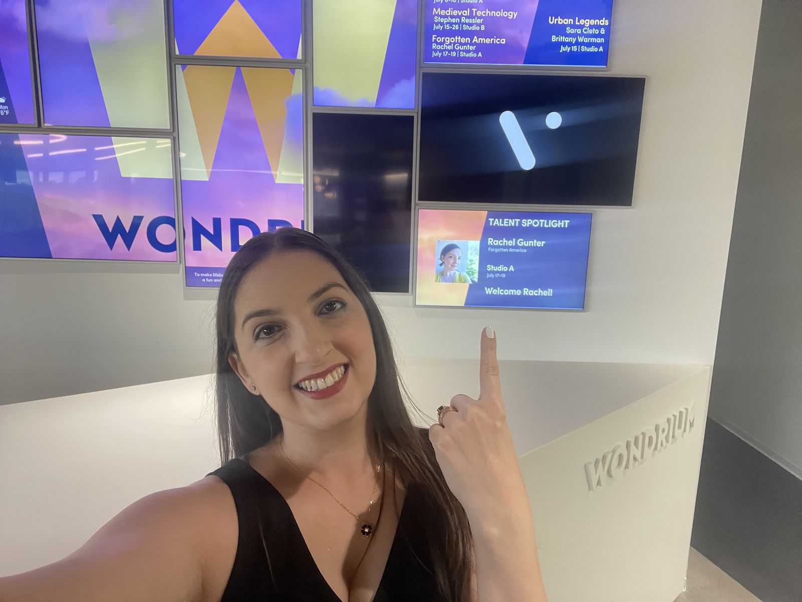 Dr. G. in a black dress in front of a set of screens that say Wondrium/The Great Courses and show her photo and name under talent spotlight. "Forgotten America" is on the filming schedule screen above. 