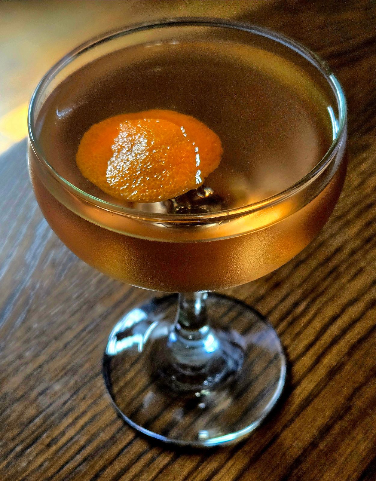 A Presidente cocktail with orange island garnish in a coupe glass sitting atop a wooden table.