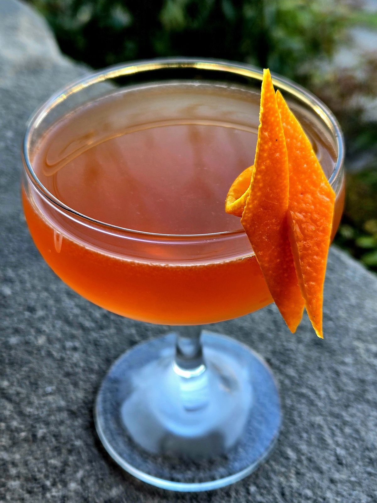 Income Tax cocktail in a Coupe with orange twist atop a stone wall.