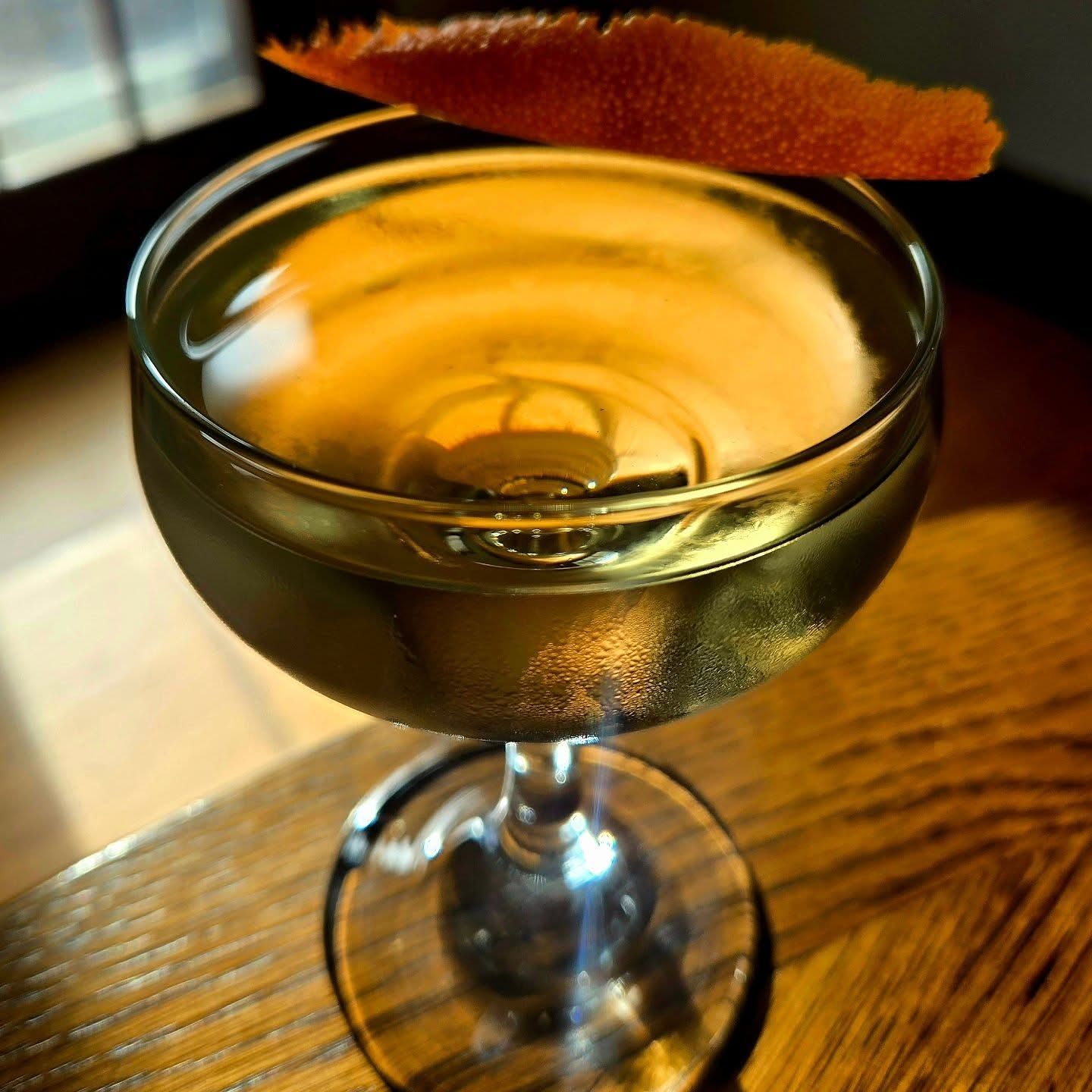 A Bamboo cocktail in a coupe glass with orange peel garnish sitting atop a wooden table.