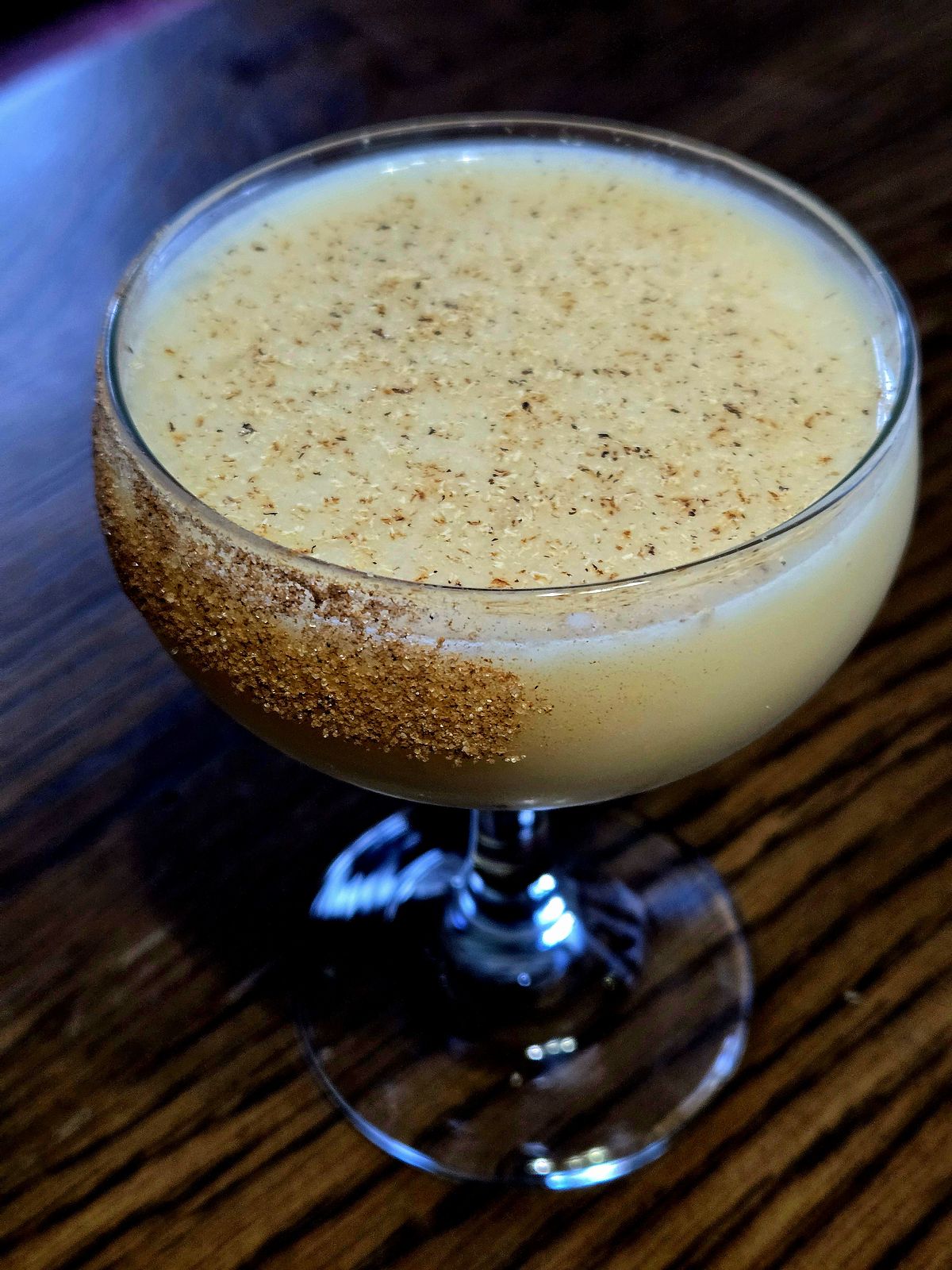 Atholl Brose cocktail in a coupe glass with cinnamon sugar rim and grated nutmeg sitting atop a wooden table.