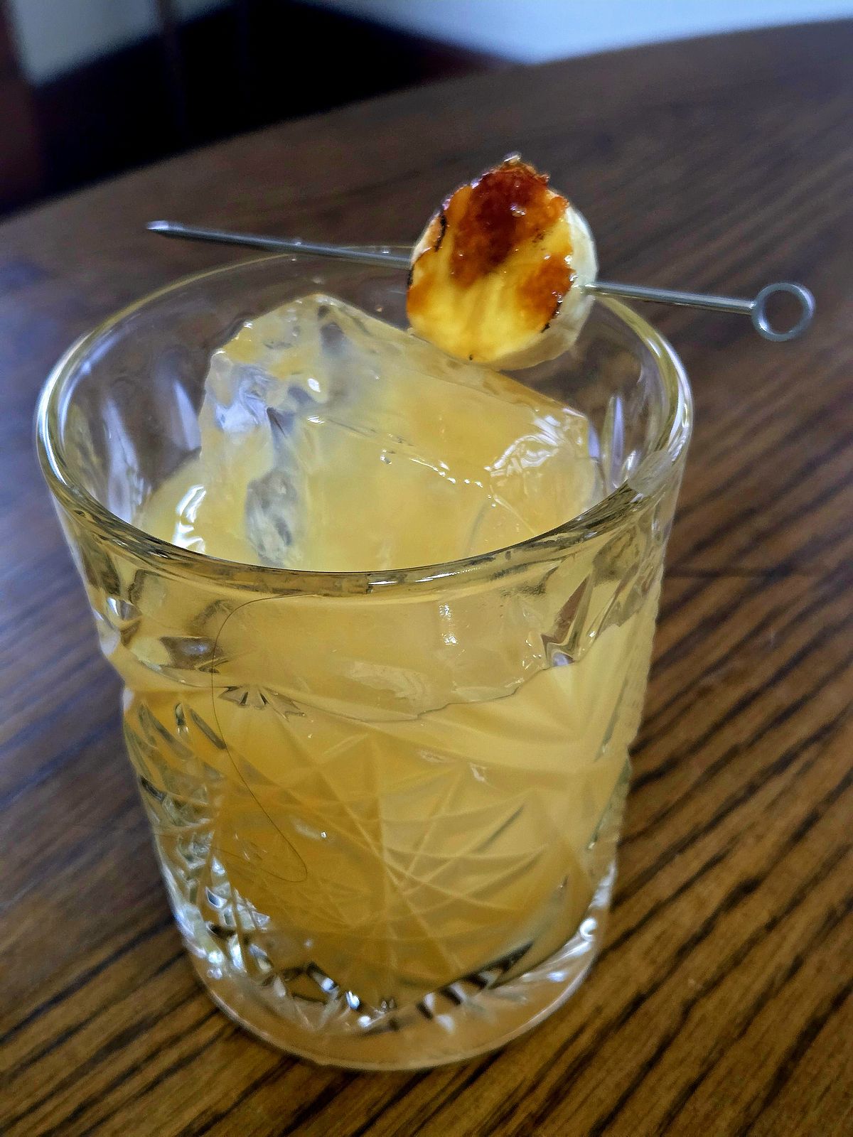 A cocktail, Without Faculty, in a rocks glass with large hand-craft ice cube and bruleed banana disk garnish. 