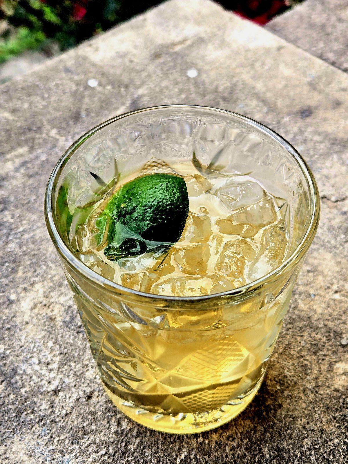 Ti' Punch with lime disc garnish in a rocks glass atop a stone wall.