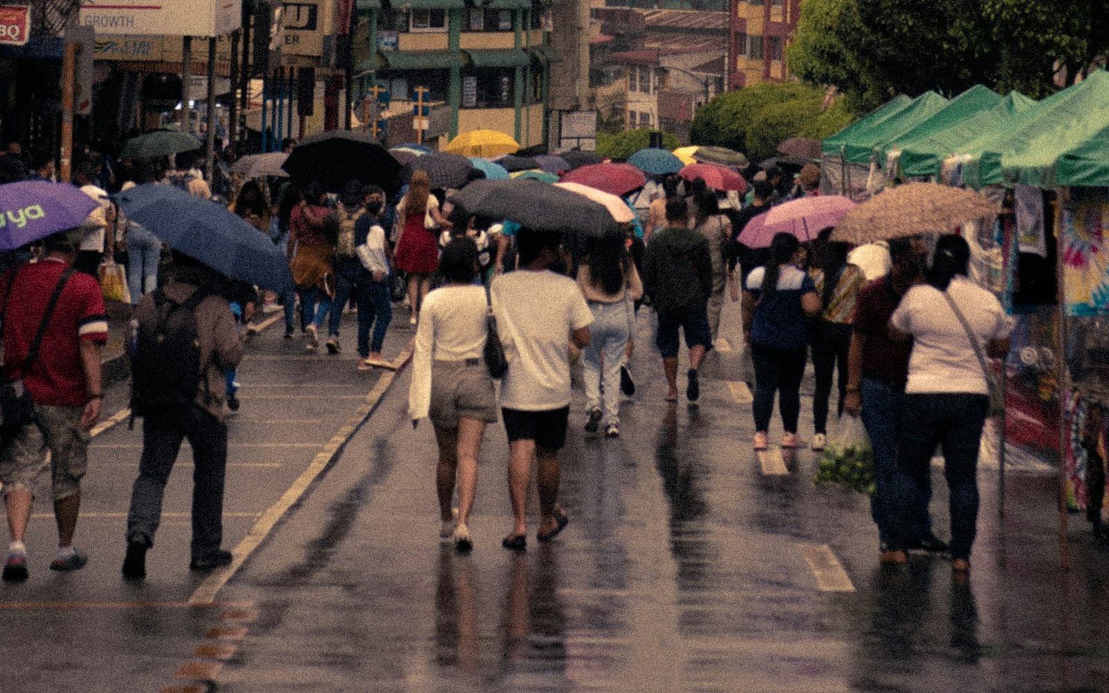 Pedestrians with umbrellas walking along a wet Session Road, Baguio, past market stalls