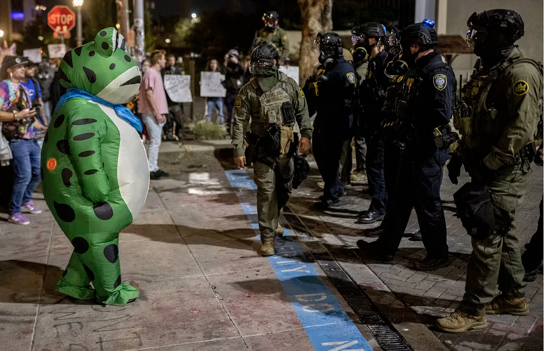 Person in inflatable frog costume facing off with armed ICE agents