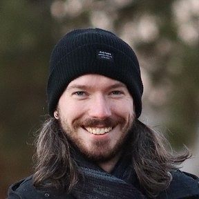 A headshot of John Bovard with foliage in the background.