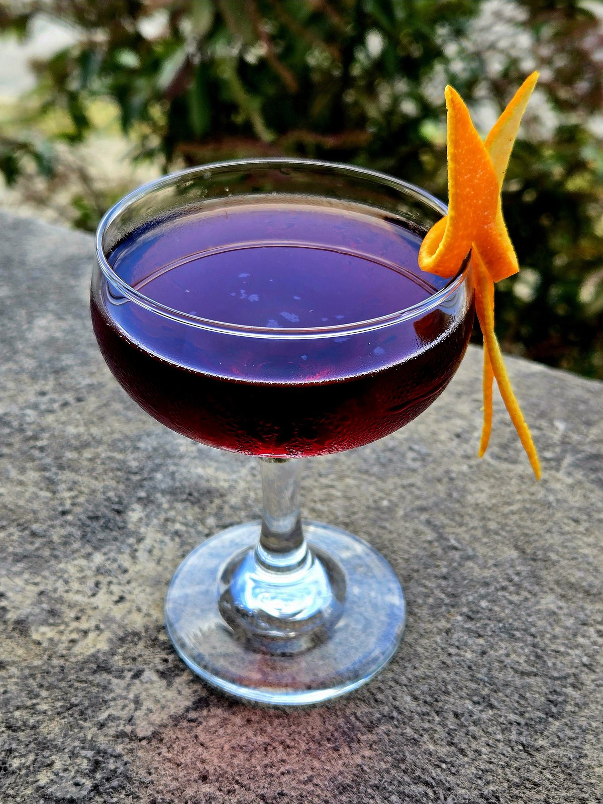 The Tipperary cocktail in a Coupe with orange twist garnish sitting atop a stone wall.