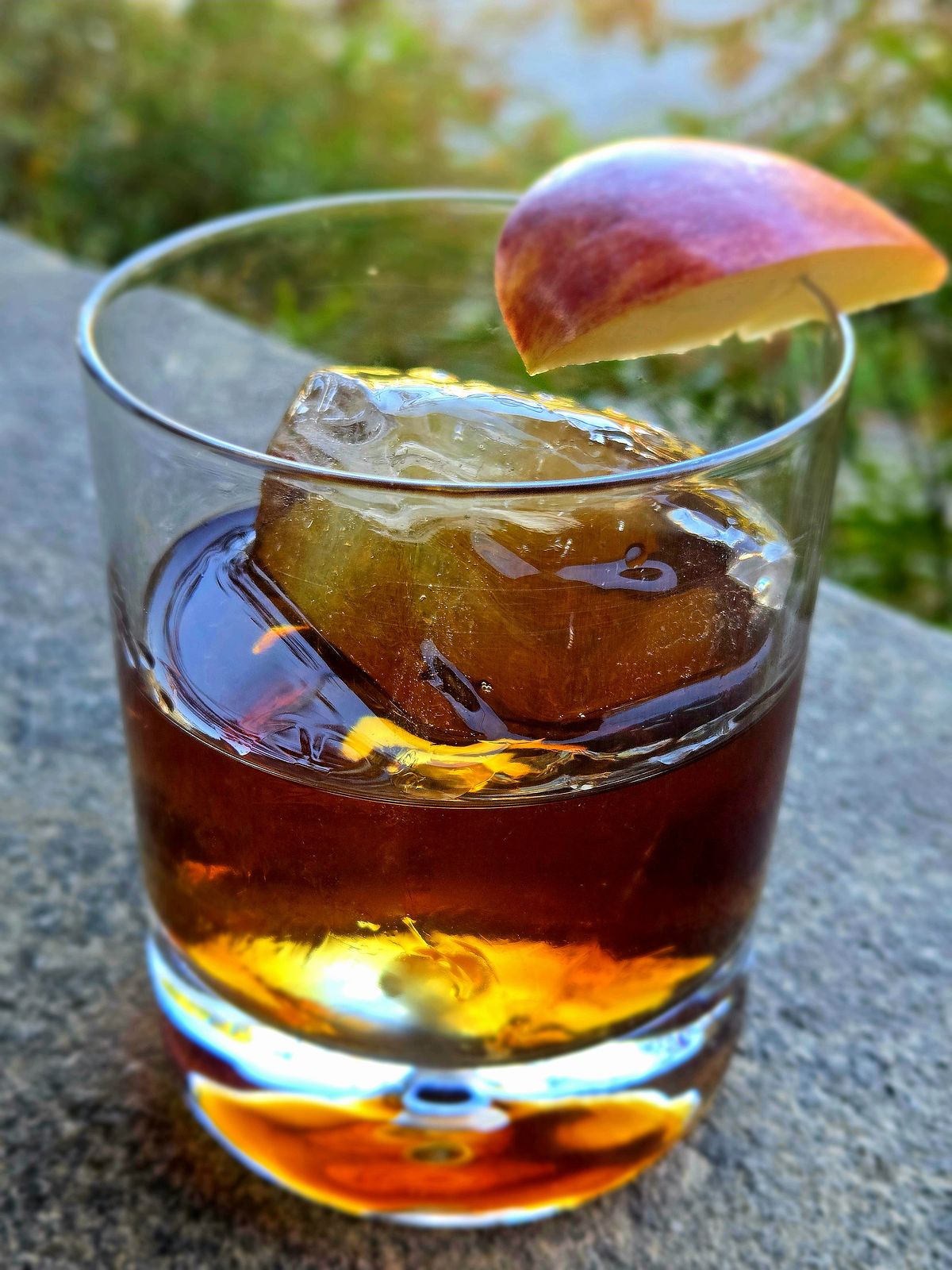 Festival Apple cocktail in a rocks glass with apple wedge garnish atop a stone wall.