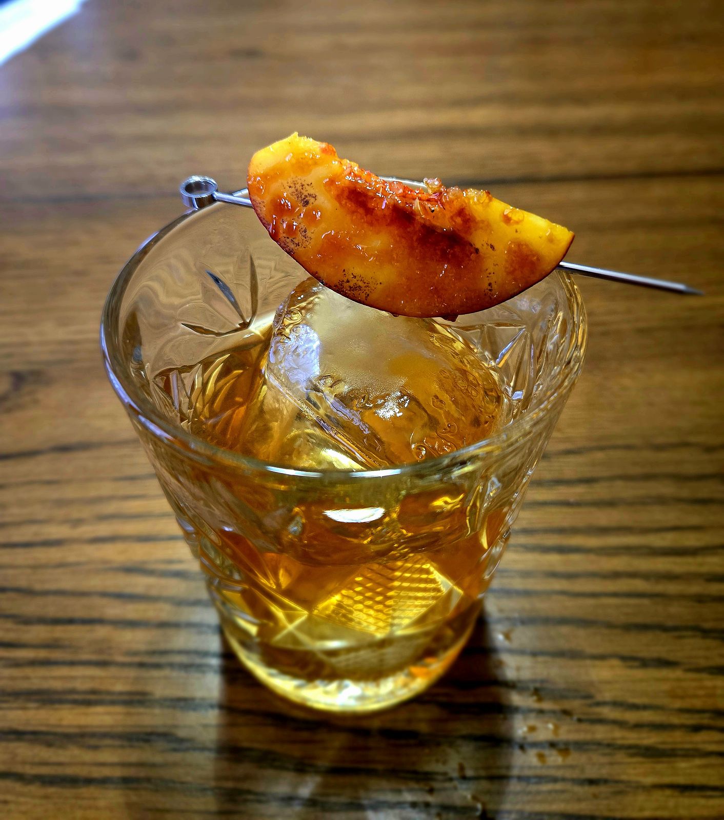 Tom's Tiki Triple rum old-fashioned with brûléed peach garnish in a rocks glass atop a wooden table. 