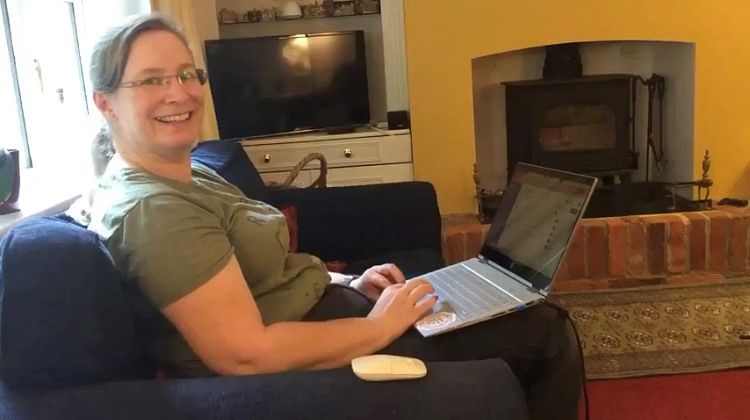 Lady with a big smile on her face looking at the camera with a laptop open on her knees.