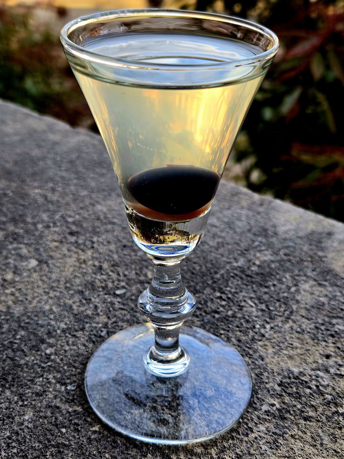 The Last Word cocktail in a cordial glass with cherry garnish atop a stone wall.
