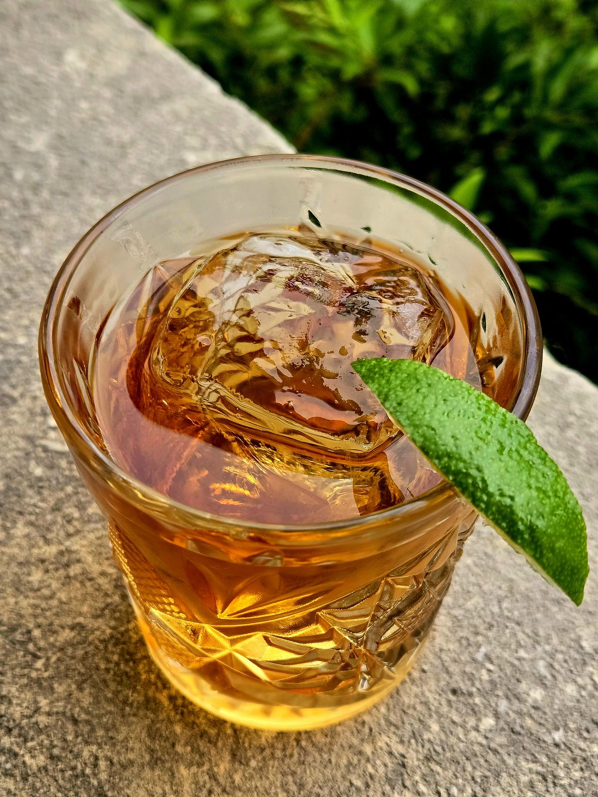 Corn 'n Oil in a rocks glass with lime sliver garnish atop a stone wall.