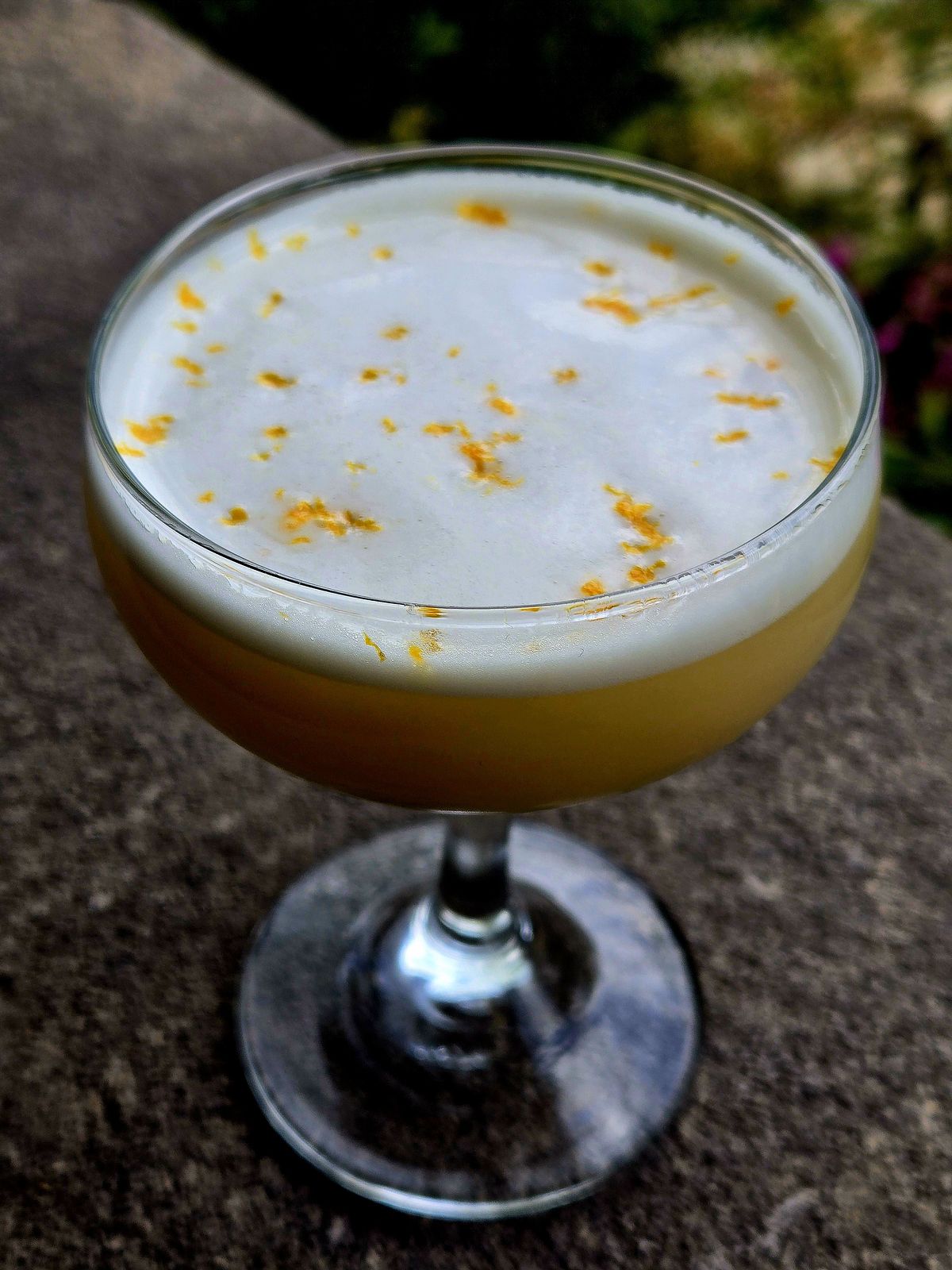 Sunset on the Charles in a Coupe with orange zest garnish atop a stone wall.