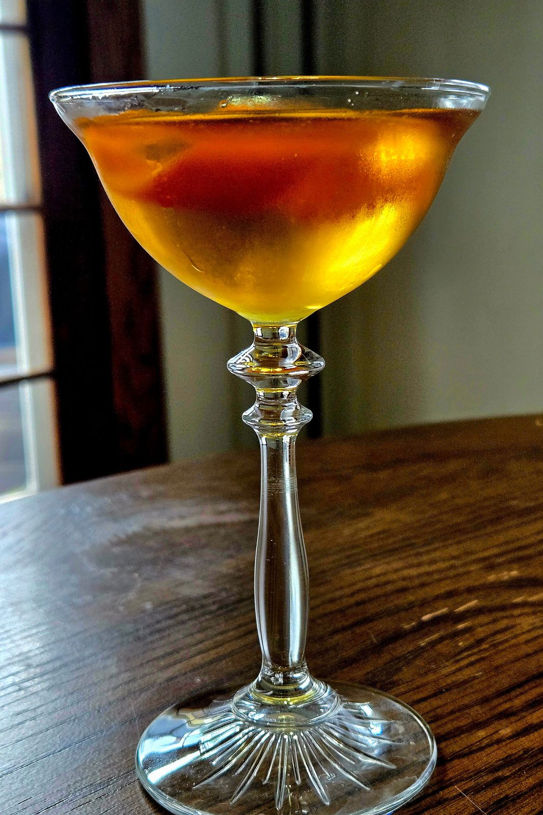 An Angel Face cocktail sitting in a coupe glass with orange twist in profile view.