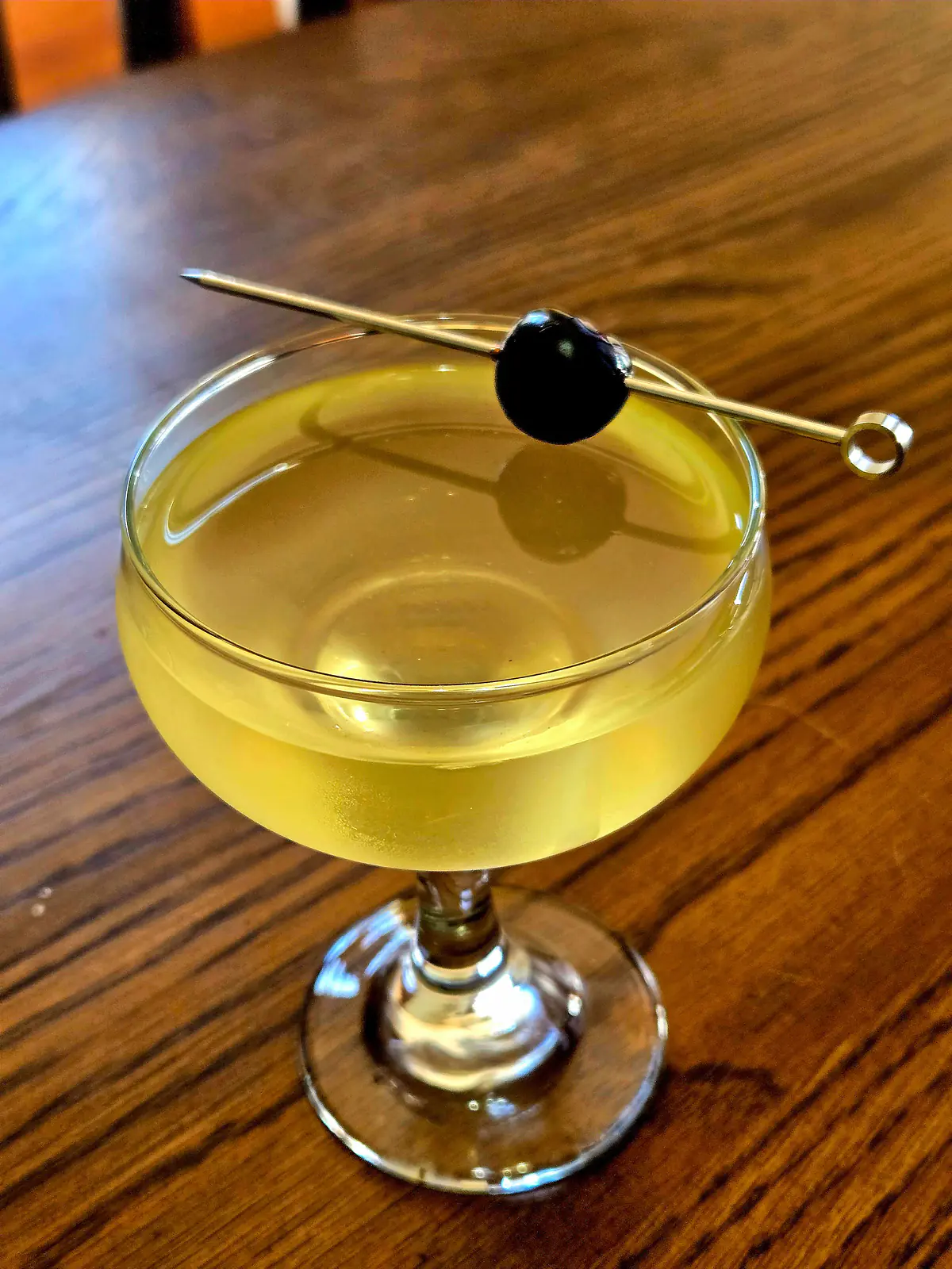 Orange Oracle in a coupe glass with Luxardo cherry garnish atop a wooden table