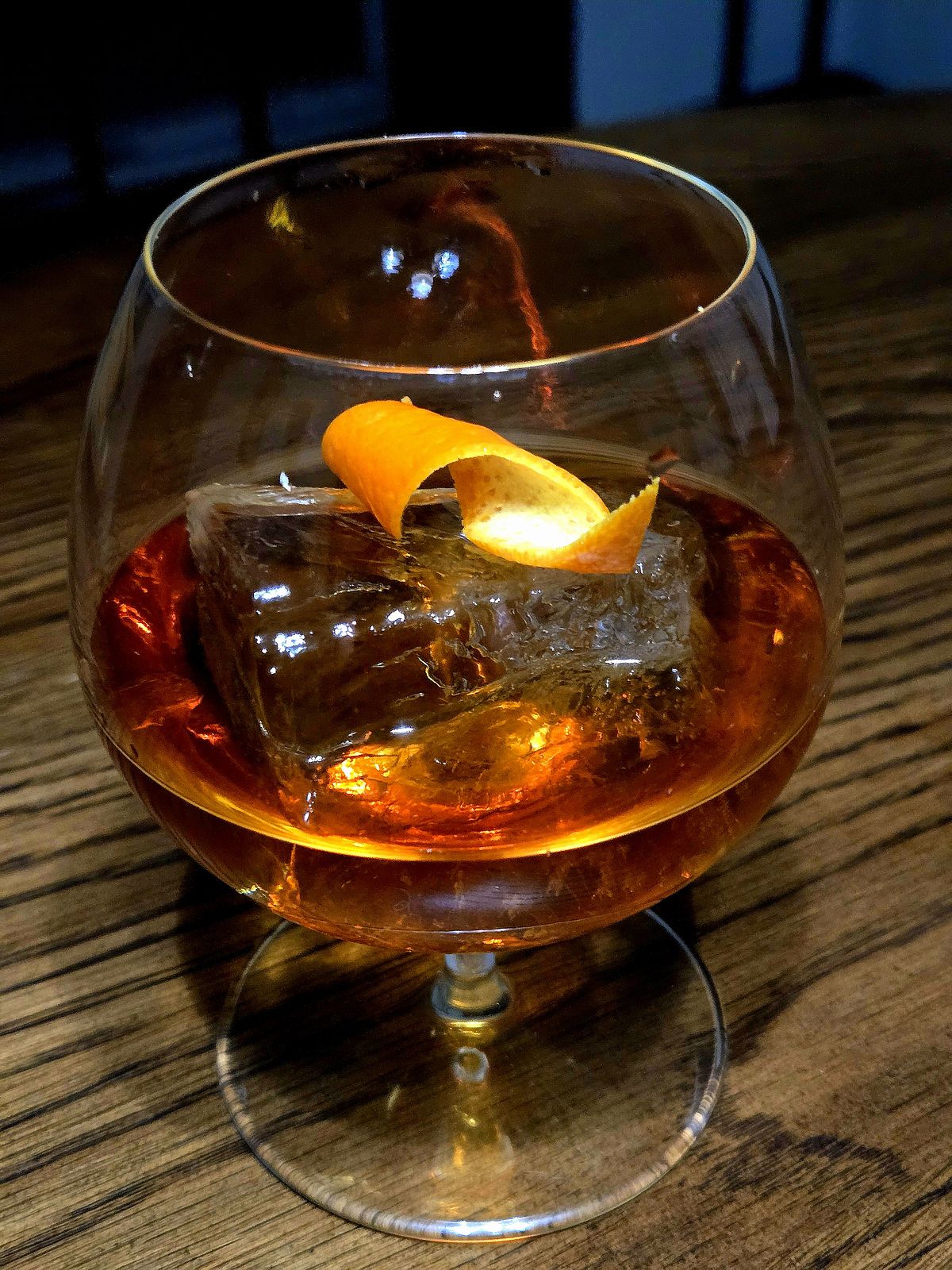 Auld Alliance cocktail with orange twist garnish in a brandy snifter atop a wooden table.