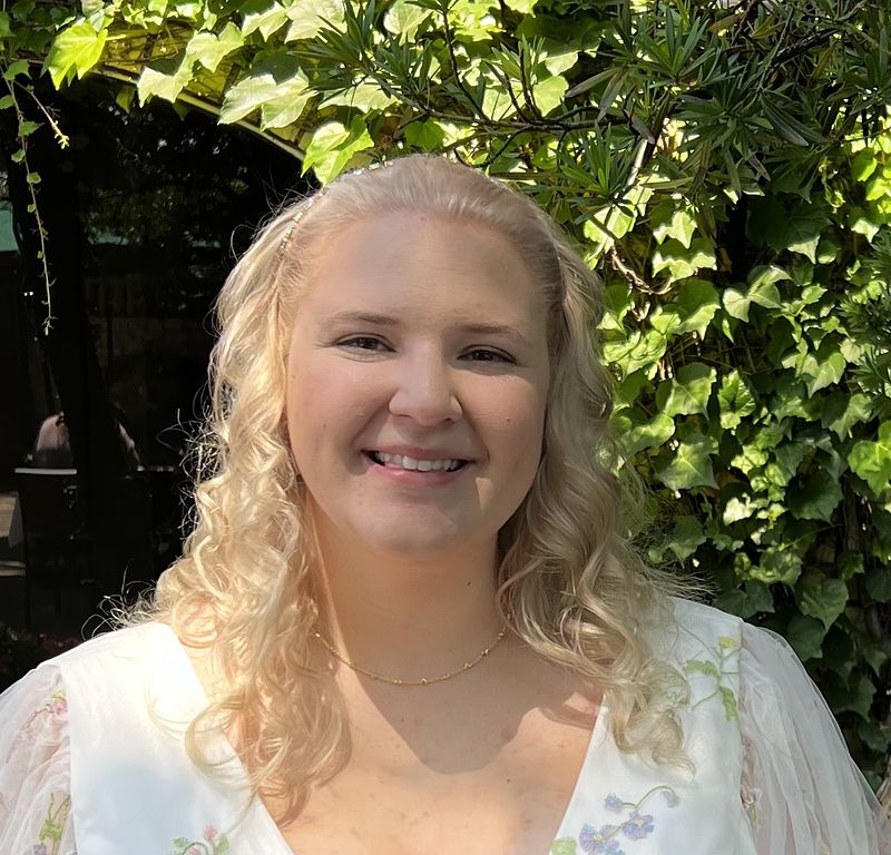 A headshot of Rebecca Moore with green leaves in the background