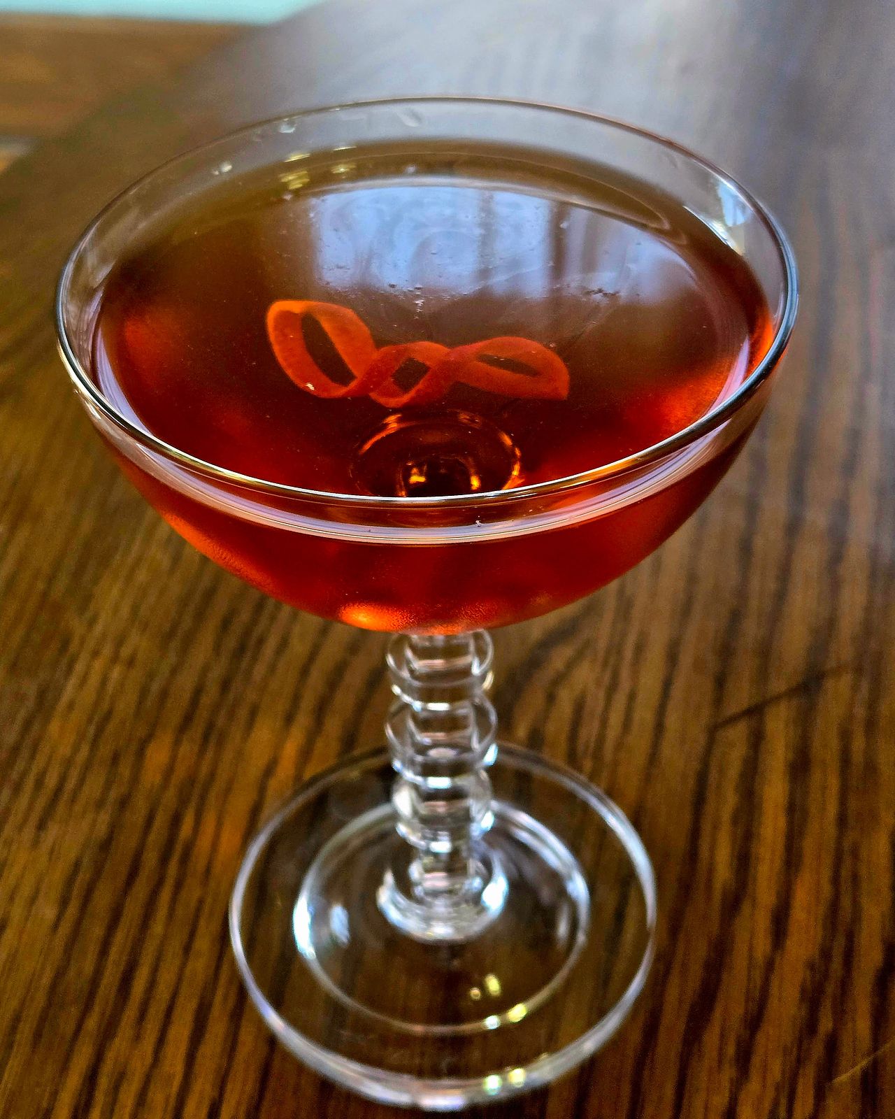 An Adonis cocktail in a champage coupe with orange lattice garnish atop a wooden table.