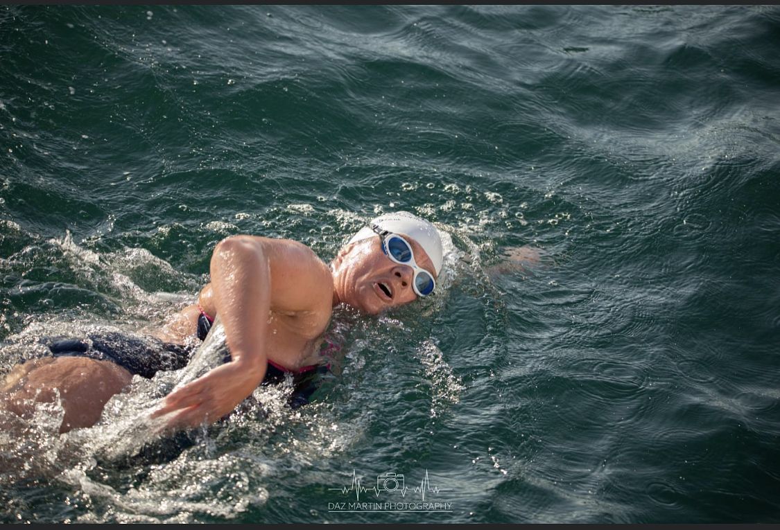 Picture of a female swimmer (Verity) in the choppy sea with a white hat and blue goggles breathing to the side as her arm comes over