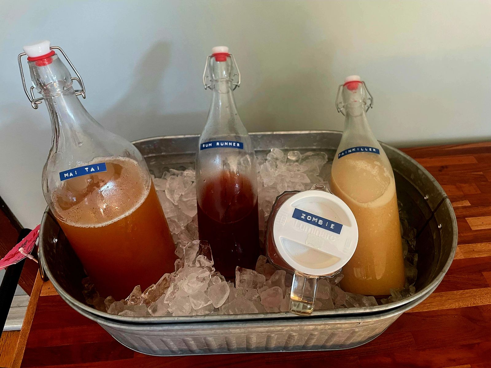 Mai Tai, Rum Runner, Zombie, and Painkiller batched cocktails in an ice tub for atop a butcher block cart.