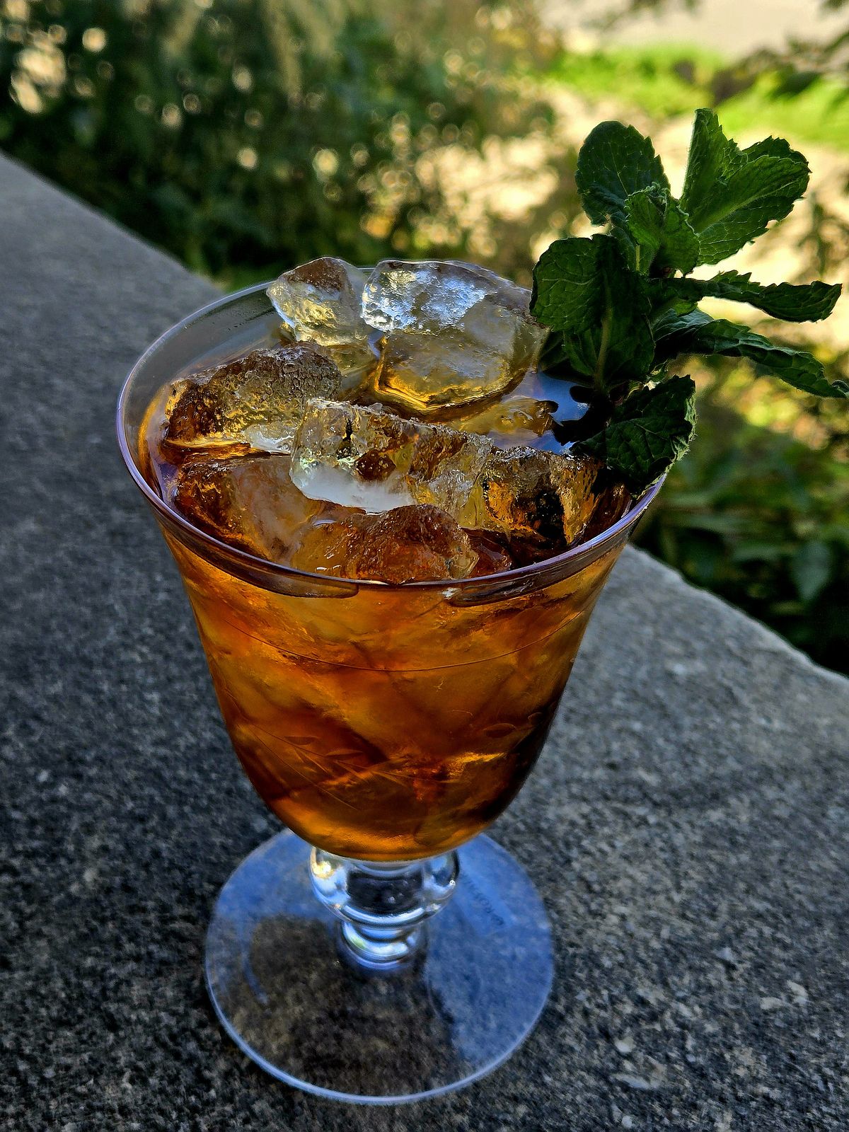 Big Red (a Mint Julep) in a vintage wine glass with mint sprig garnish atop a stone wall.