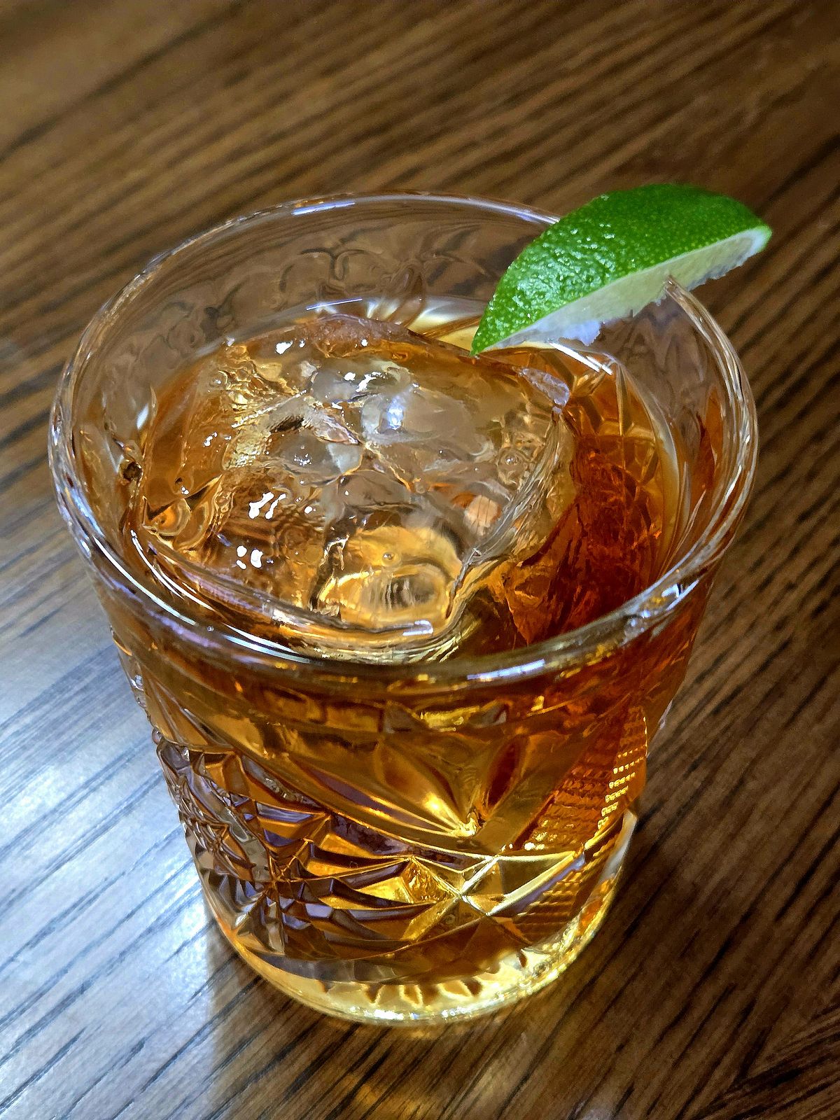 Corn 'n Oil in a rocks glass with lime sliver garnish atop a wooden table.