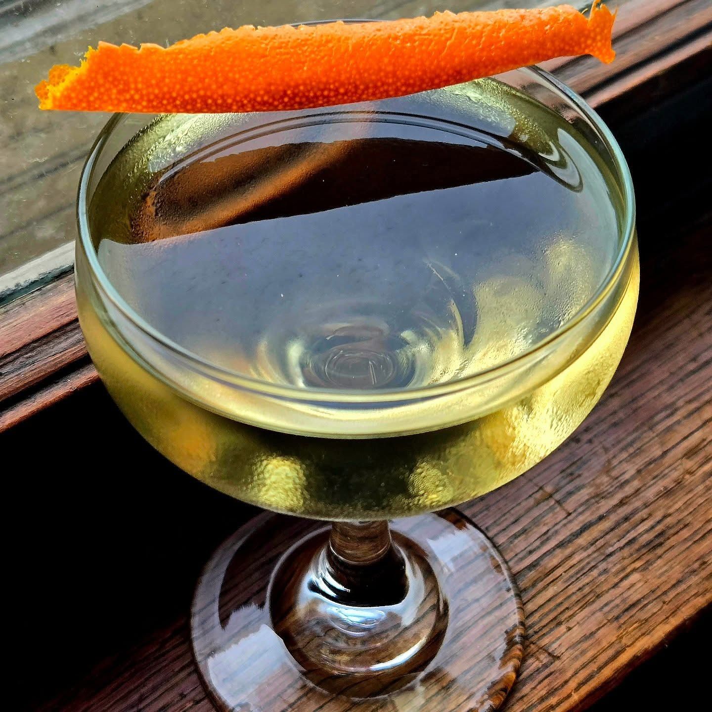 A Bamboo cocktail in a coupe glass with orange peel garnish sitting in a window seal.