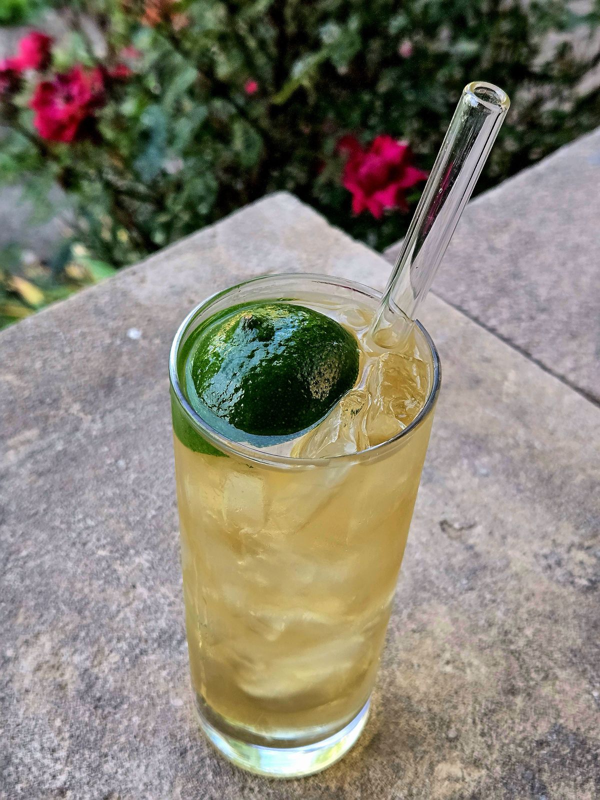 Ti' Punch highball with lime disc garnish and straw atop a stone wall.