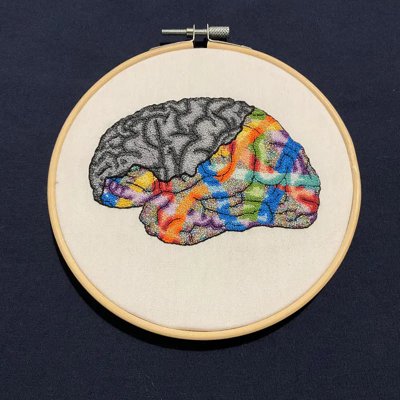 Embroidery depicting the process of unmasking neurodivergence even in the face of societal pressure to feign neurotypicality.