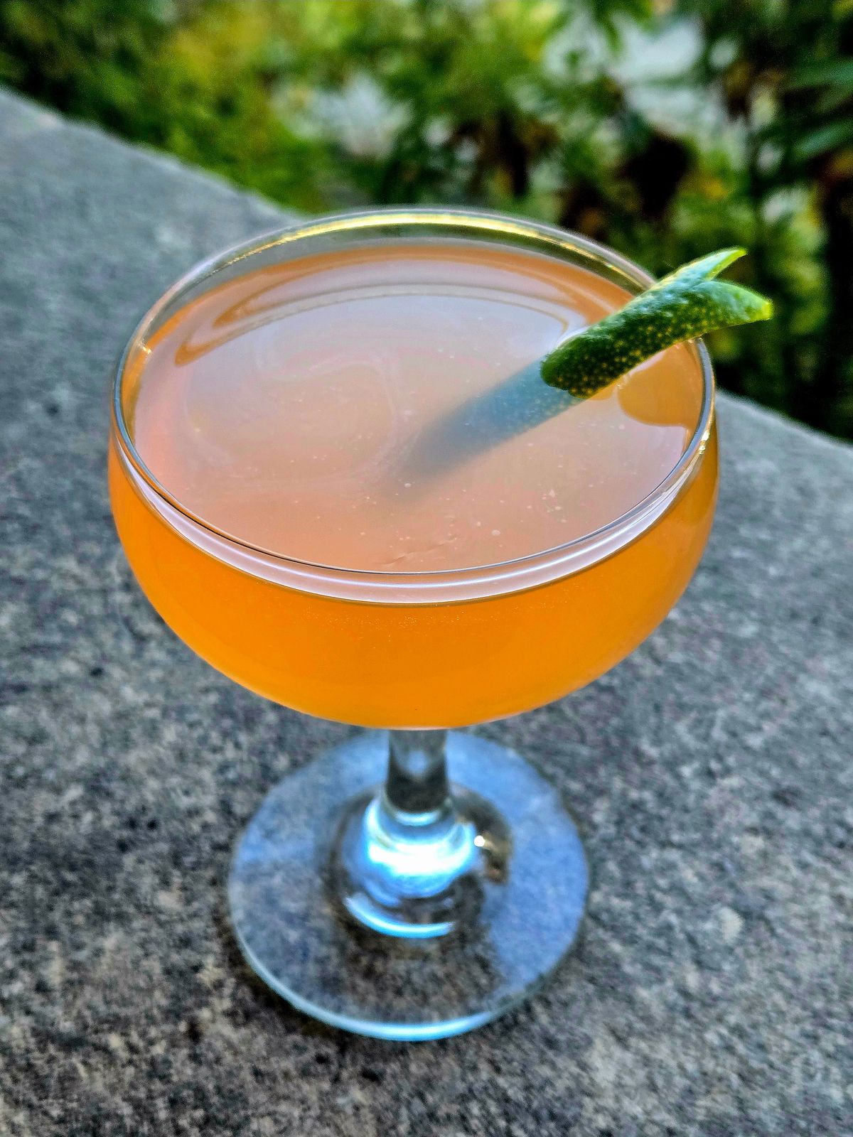 A Pegu Club cocktail in a couple glass with lime lapel garnish sitting outdoors on stone.