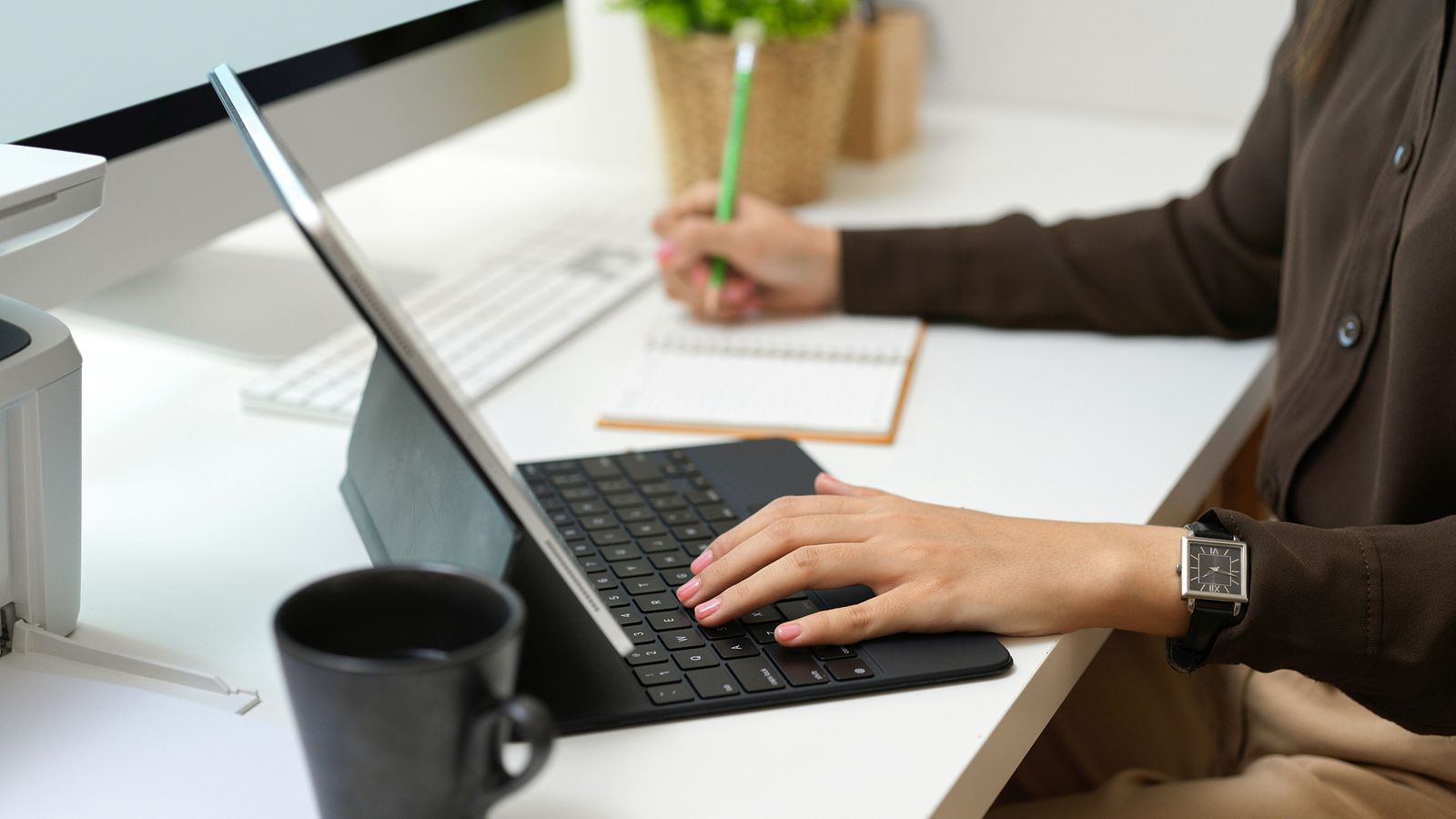 A person writing notes beside a laptop at a desk.