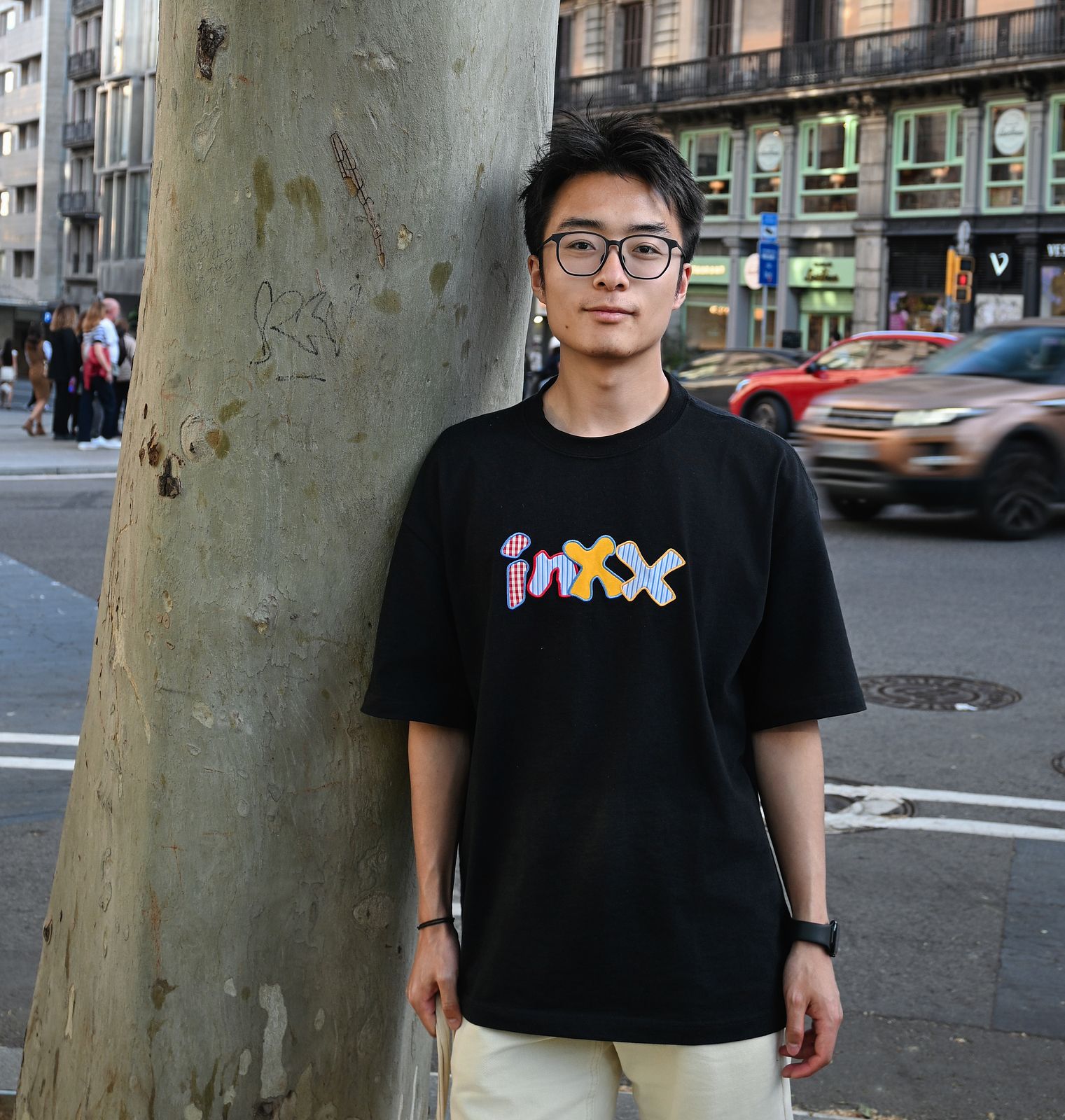 Asian male wearing glasses and a black t-shirt standing next to a tree