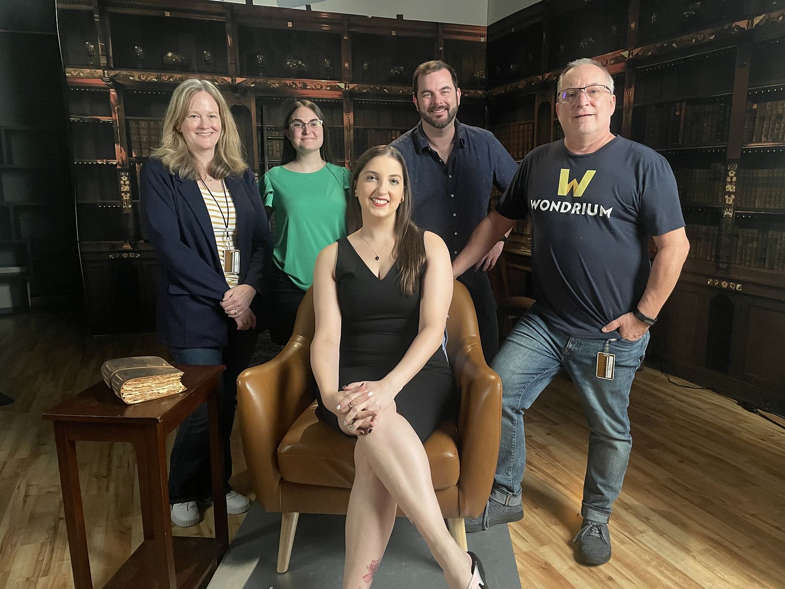 Dr. G in a black dress sitting in a brown armchair surrounded by the 4-person team behind filming Forgotten America