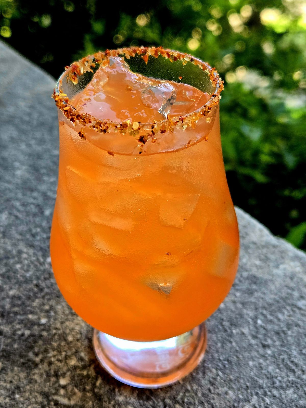 Dead Man's Handle Tequila cocktail with Tajin rim in a Glencairn glass atop a stone wall.