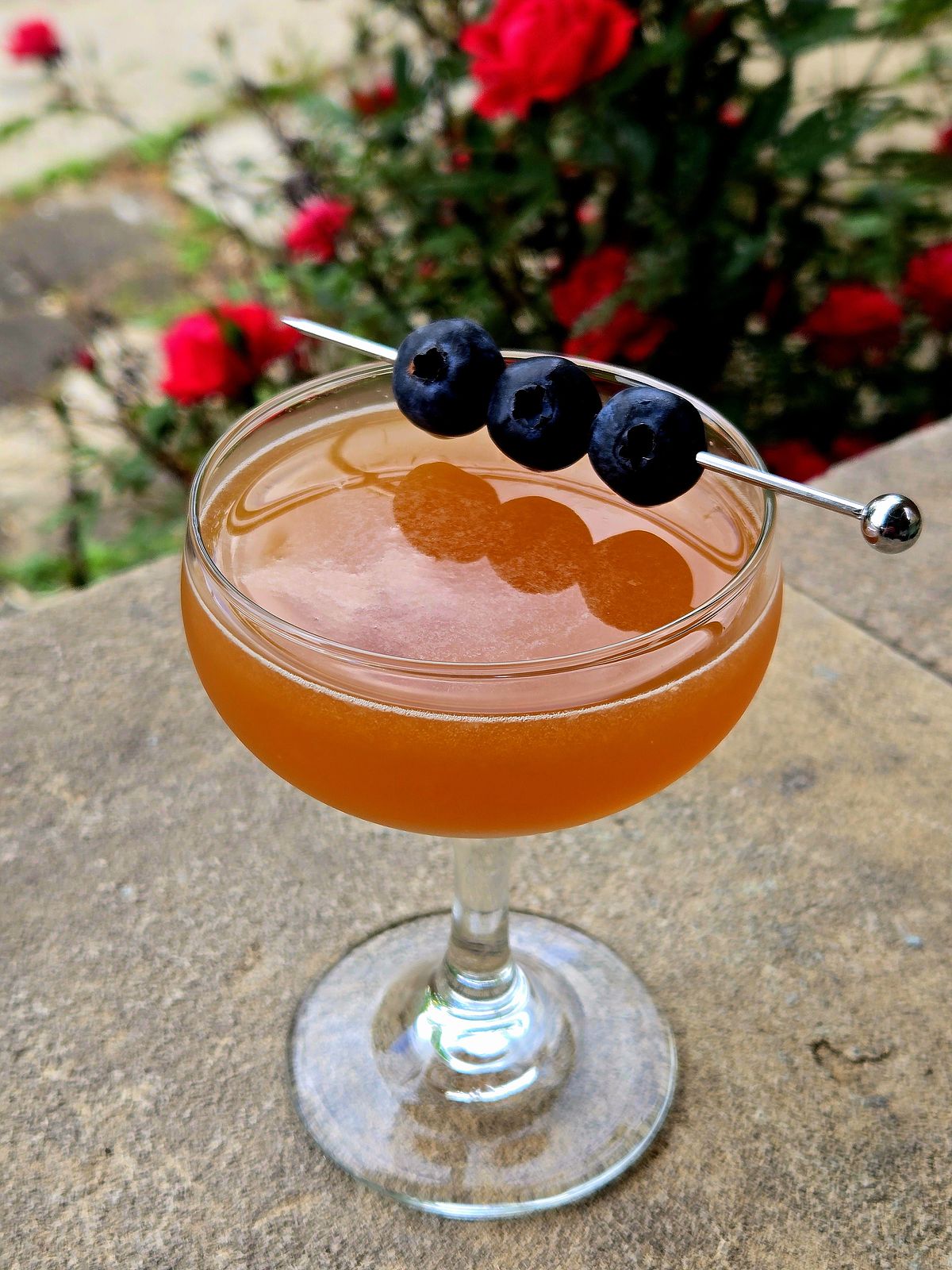 Champs-Élysées cocktail with blueberry garnish in a Coupe atop a stone wall.