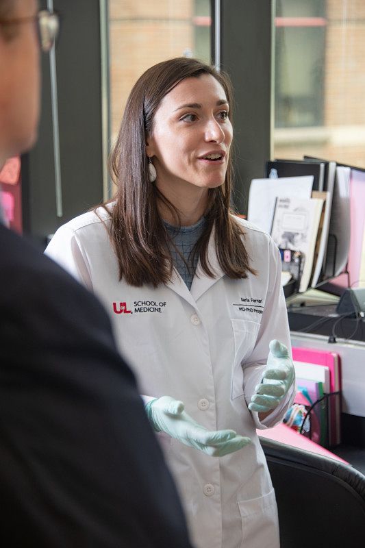 Scientist in lab coat speaking to other scientists.