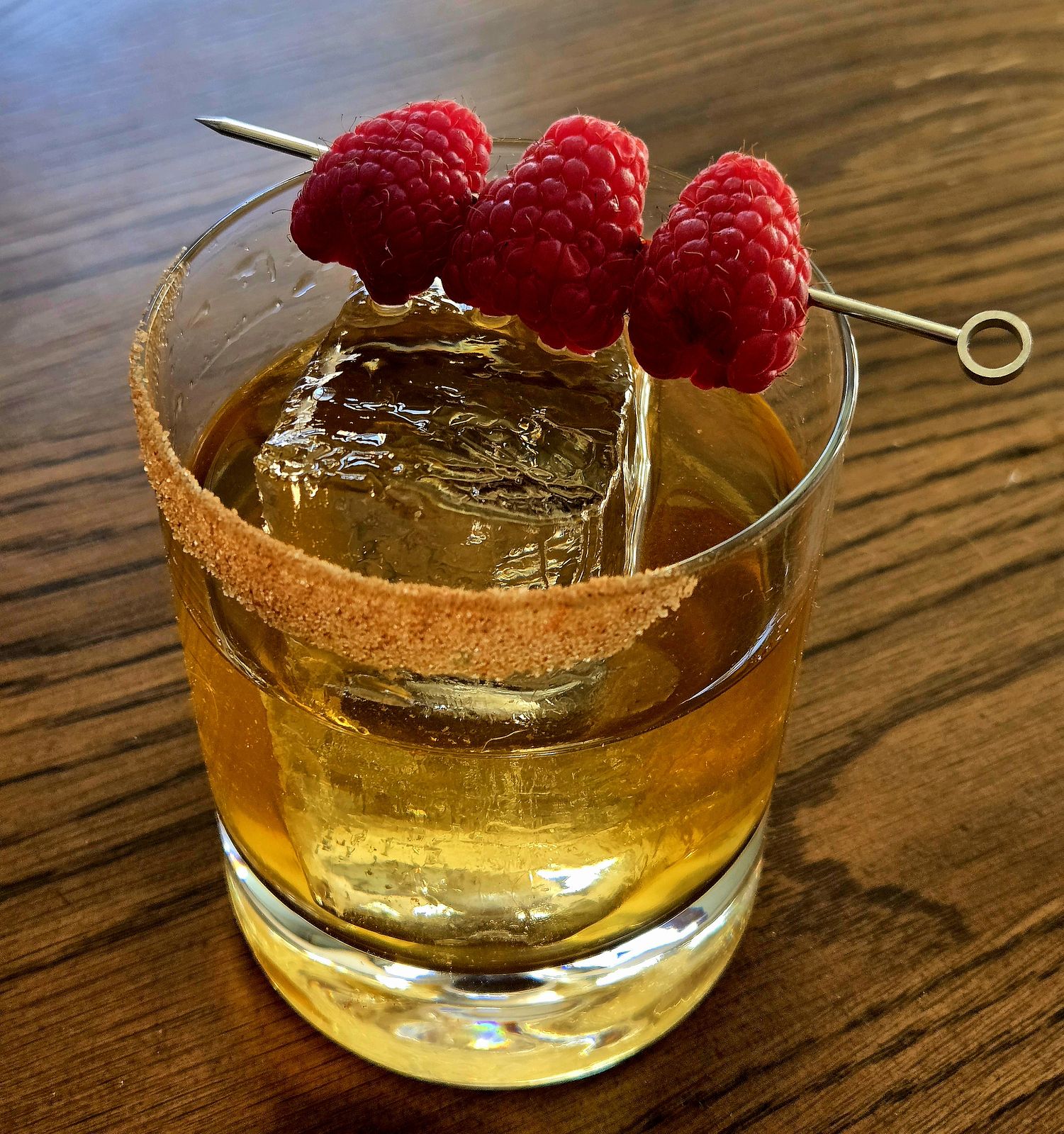 Scottish Sandie cocktail in a rocks glass with cinnamon-sugar rim and raspberry garnish atop a wooden table.