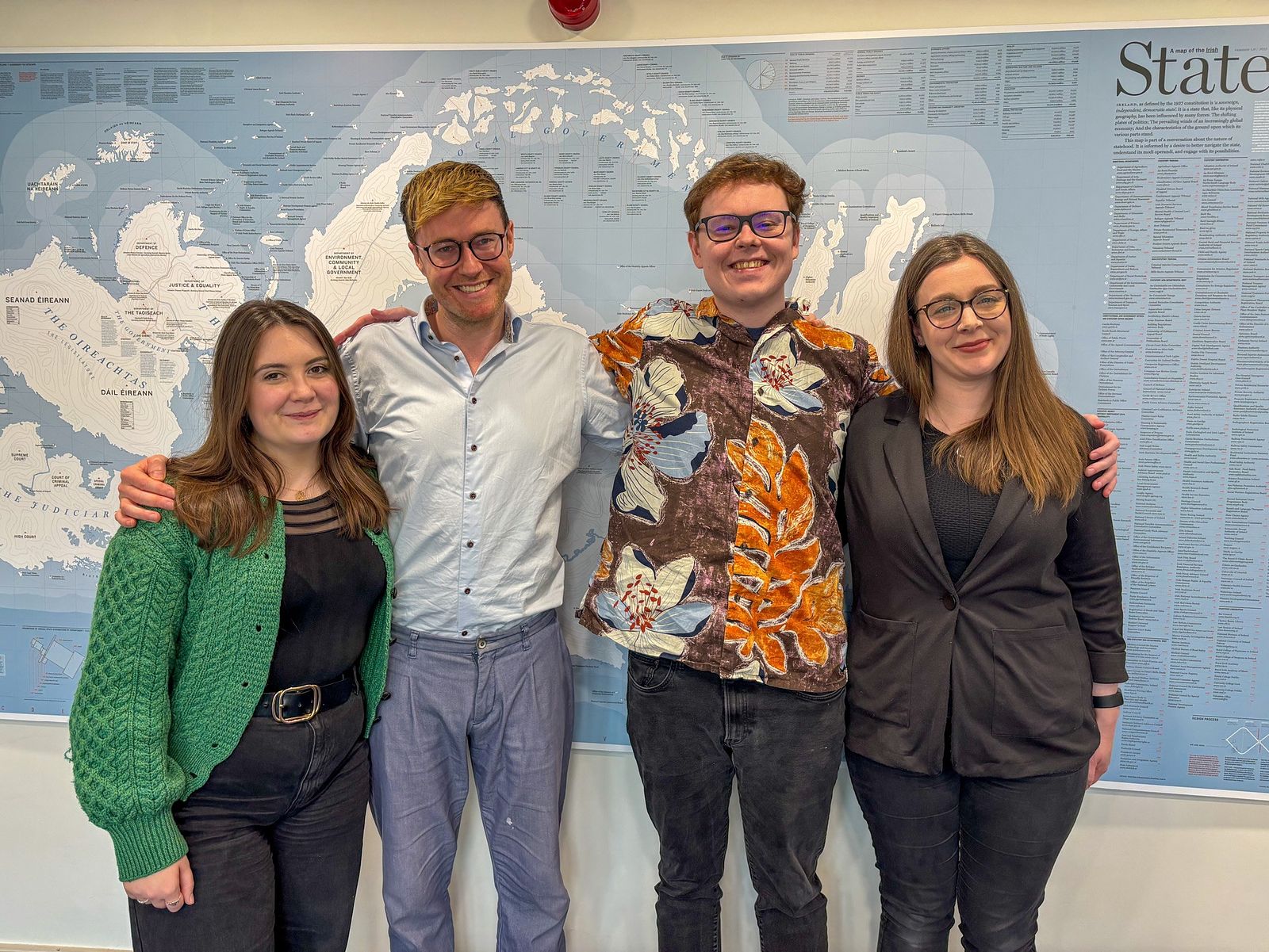 Organisers of the Interdisciplinary Writing Solidarity Group, left to right: Isabelle Nic Craith, Glen Jankowski, Pat Mulvaney and Laura Foley are pictured smiling, in front of a large map.