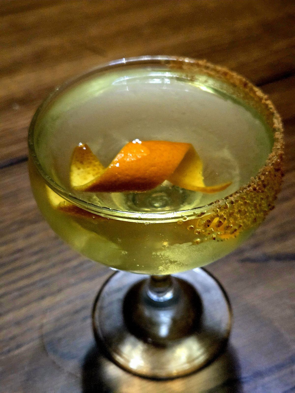 Milk-clarified Sidecar with orange twist and coconut sugar rim in a Coupe atop a wooden table.