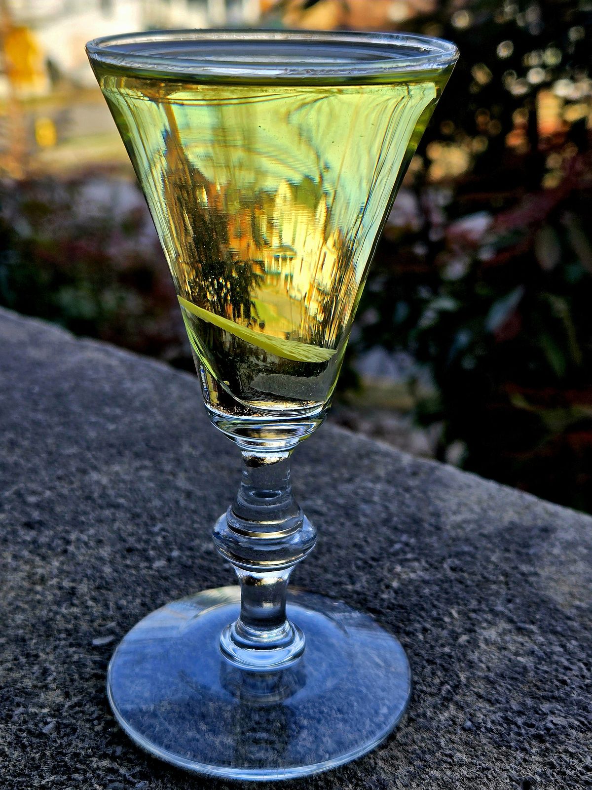 Alaska cocktail with lemon disc garnish in a sherry glass sitting atop a stone wall.