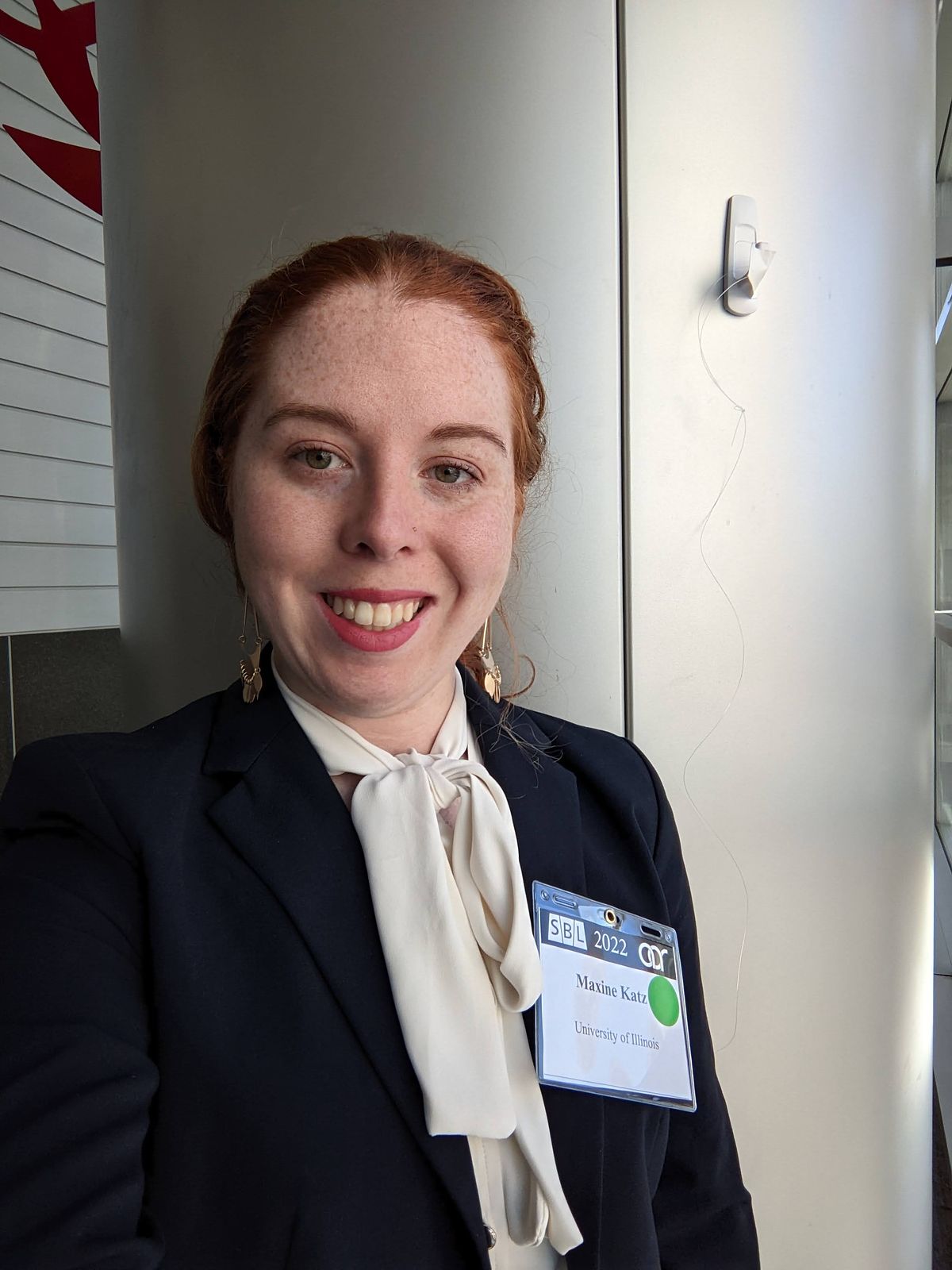 A picture of a redheaded woman in a navy blazer smiling at the camera during the American Academy of Religion annual conference in 2022. Denver, Colorado.